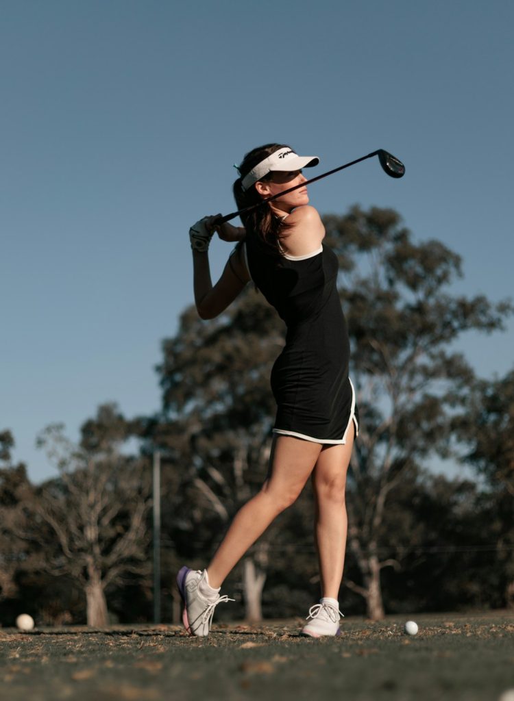 a-woman-swinging-a-golf-club-at-a-ball-ia5vnkpapys