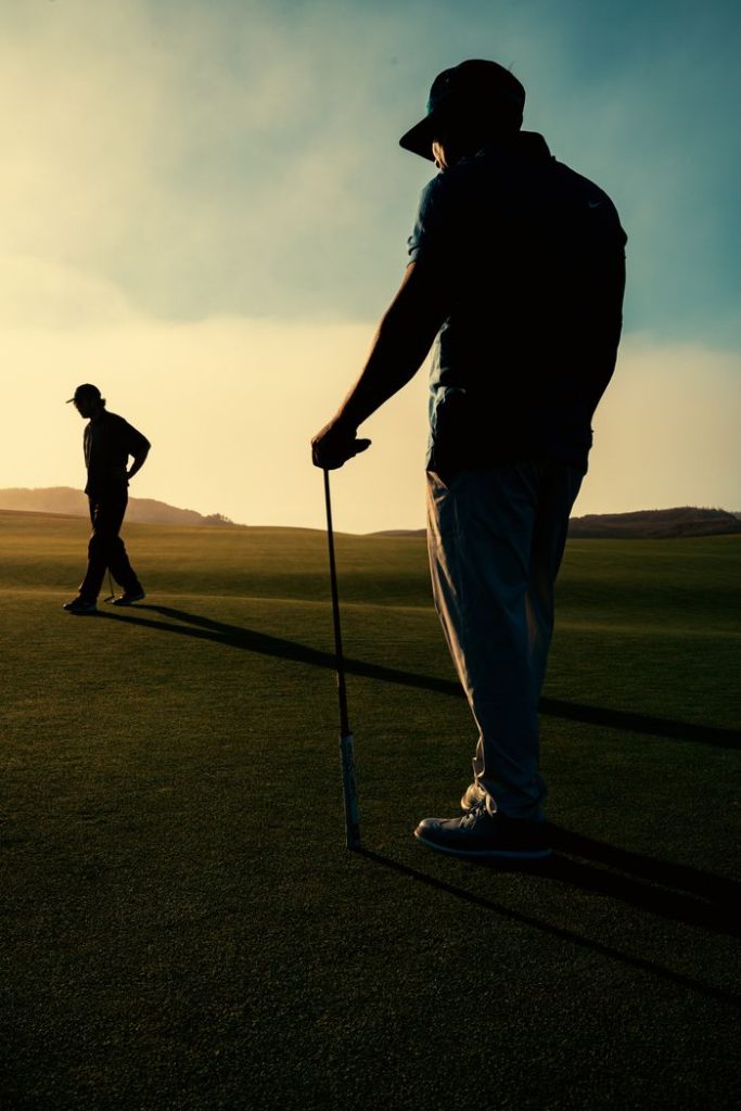 Two golfers casting long shadows on a golf course at sunset, creating a striking silhouette.