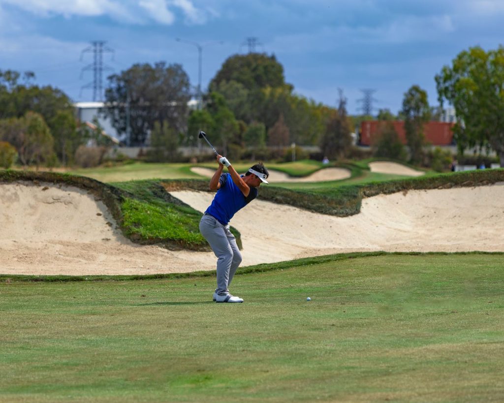 A golfer in mid-swing on a beautifully maintained golf course with clear skies and lush surroundings.